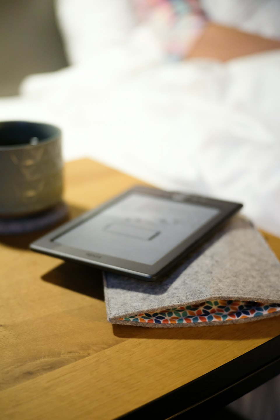 Czytnik e-booków i ceramiczny kubek na drewnianym stoliku nocnym.